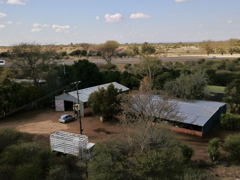 Aerial view of a small holding property featuring multiple outbuildings with corrugated metal roofs and surrounding rural landscape.