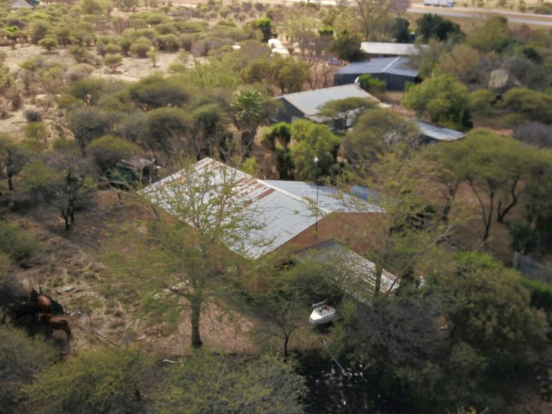 Aerial view of a small holding property featuring multiple structures with corrugated metal roofing situated within a wooded landscape.