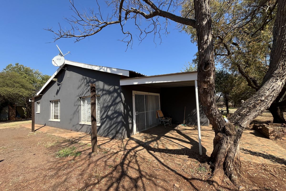 Rear view of the property featuring a covered patio area with tiled flooring, security gates, and established trees in the surrounding garden.
