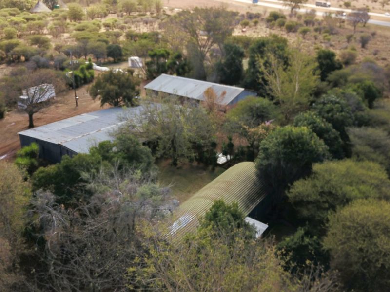 Aerial view of a small holding property featuring multiple outbuildings with corrugated metal roofs situated within a rural, wooded landscape.