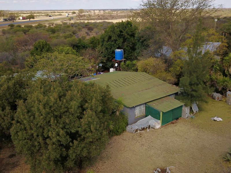 Aerial view of a small holding property featuring a main dwelling with a metal roof, water storage tank, and surrounding garden area.