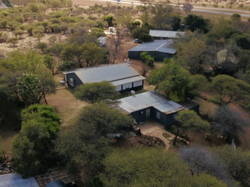 Aerial view of a small holding property featuring multiple structures with corrugated metal roofing set within a large, tree-filled landscape.