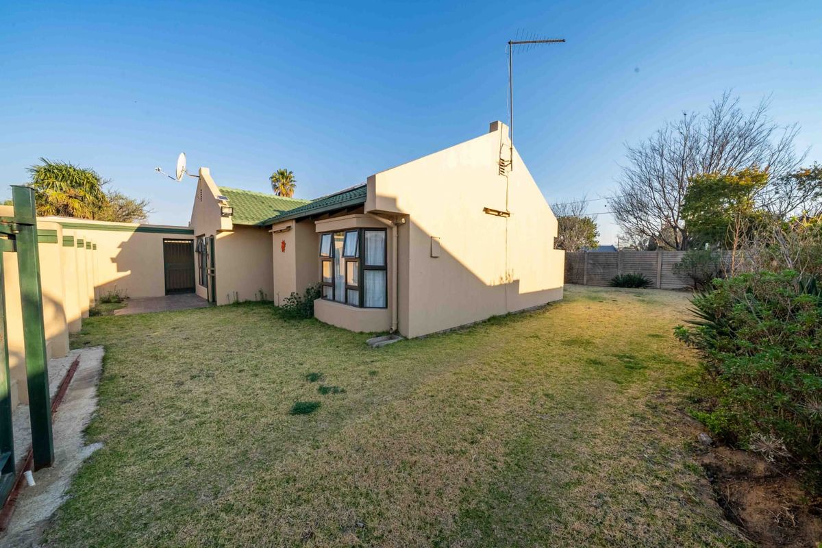 Rear view of the property featuring a bay window, tiled roof, and a spacious garden area enclosed by a precast concrete boundary wall.