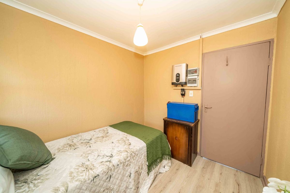 A compact bedroom featuring laminate flooring, coving, and wall-mounted electrical infrastructure including an inverter system.
