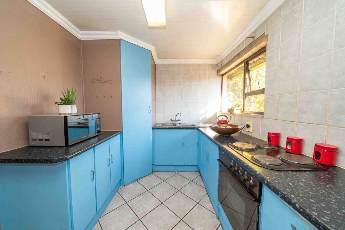 A functional kitchen featuring blue cabinetry, dark laminate countertops, a built-in oven with electric hob, and tiled backsplash and flooring.