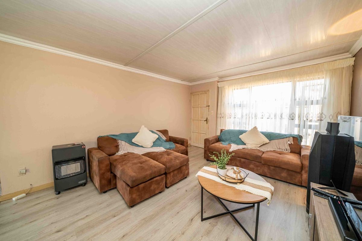 A living room featuring light-toned laminate flooring, coved ceilings, and a large window allowing natural light into the space.