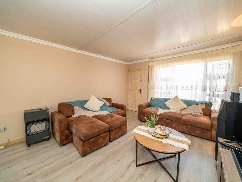 A living room featuring light-toned laminate flooring, coved ceilings, and a large window allowing natural light into the space.