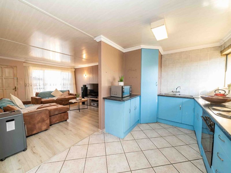 Open-plan living area featuring a kitchen with blue cabinetry, built-in oven, and tiled flooring, seamlessly flowing into a comfortable lounge space.
