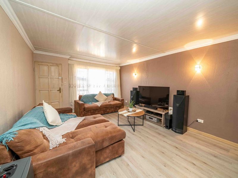 A comfortable living room featuring light-toned laminate flooring, textured walls, and a panelled ceiling with integrated wall sconce lighting.