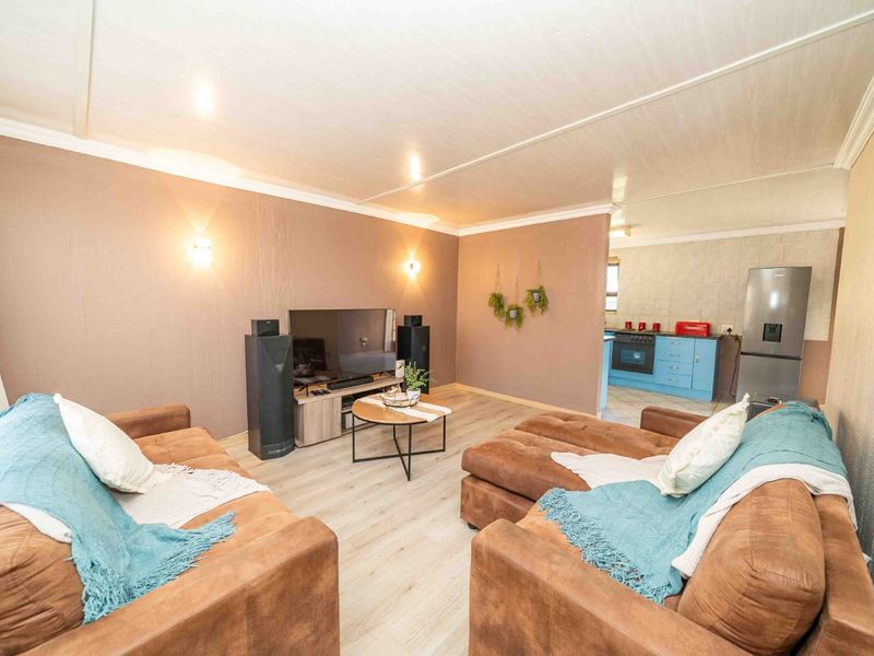Open-plan living area featuring light laminate flooring, wall-mounted lighting, and an adjoining kitchen space with blue cabinetry and built-in cooking appliances.