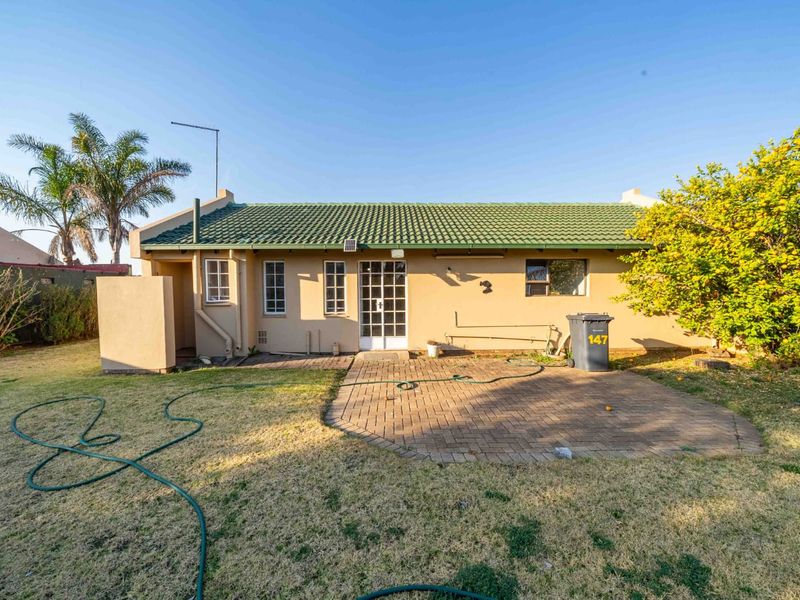Rear view of the property featuring a paved patio area, green tiled roof, and established garden space.