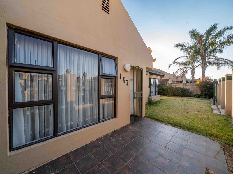 Front exterior view of the property featuring a tiled patio, security gate, and well-maintained lawn area.