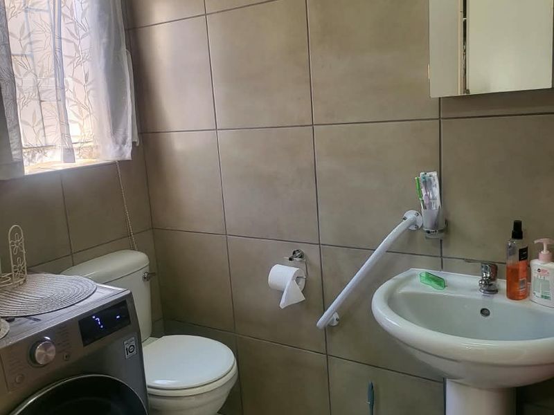 A functional bathroom featuring tiled walls, a pedestal basin with a grab rail, and a toilet, with space for a laundry appliance.