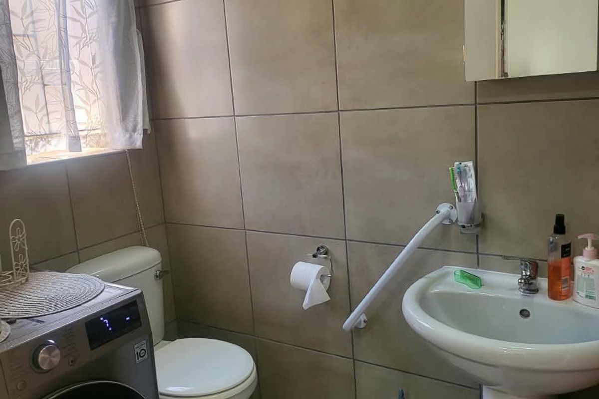 A functional bathroom featuring tiled walls, a pedestal basin with a grab rail, and a toilet, with space for a laundry appliance.