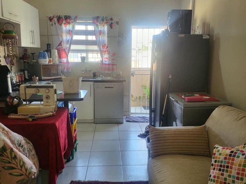 Open plan living and kitchen area featuring tiled flooring, functional cabinetry, and direct access to an exterior door with security gate.
