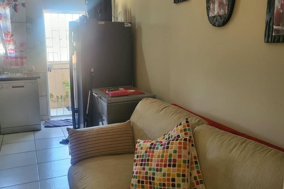 An open-plan living area featuring tiled flooring and direct access to an exterior space through a security gate.