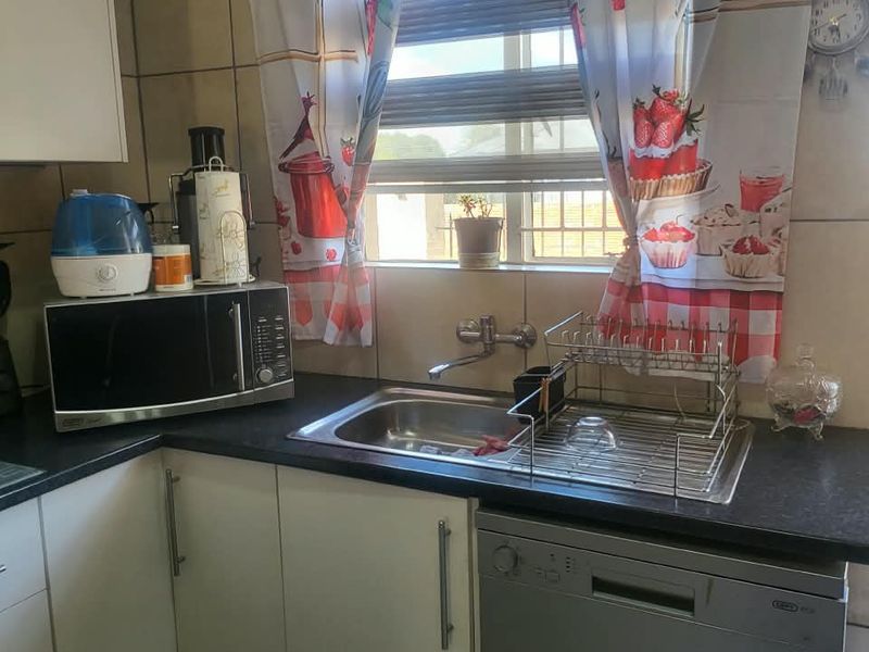A functional kitchen area featuring built-in cabinetry, a stainless steel sink with mixer tap, tiled splashback, and tiled flooring.