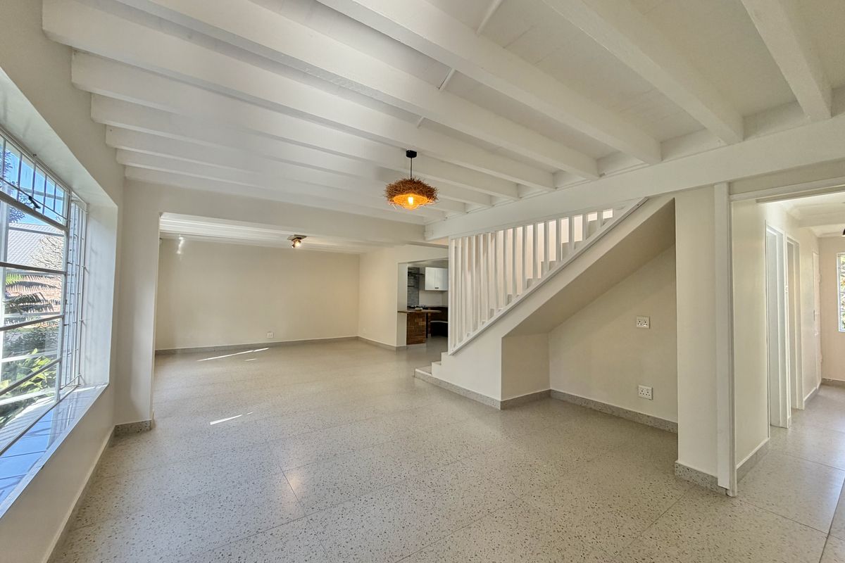 Spacious open-plan living area featuring exposed beam ceilings, terrazzo flooring, and a central staircase, offering a bright and neutral canvas.