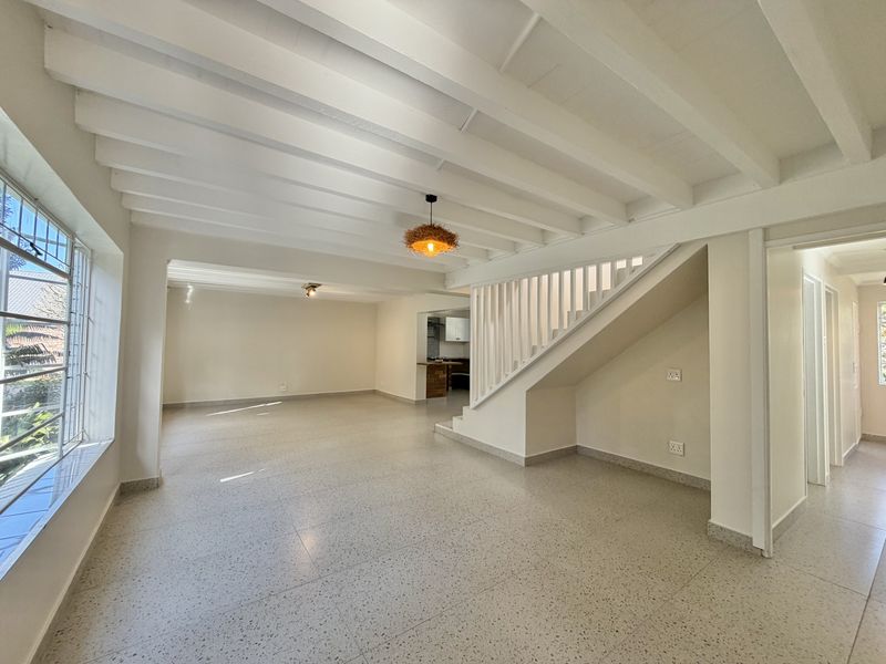 Spacious open-plan living area featuring exposed beam ceilings, terrazzo flooring, and a central staircase, offering a bright and neutral canvas.