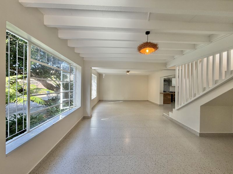 Spacious open-plan living area featuring exposed white ceiling beams, modern terrazzo flooring, and a staircase, offering a bright and versatile layout.