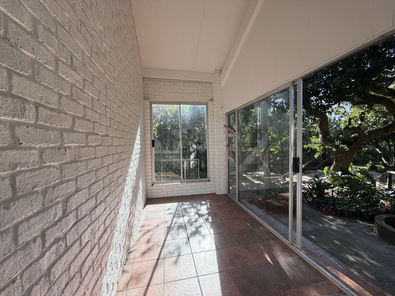 A bright, covered patio area featuring painted brick walls, tiled flooring, and large sliding glass doors that open onto a garden view.
