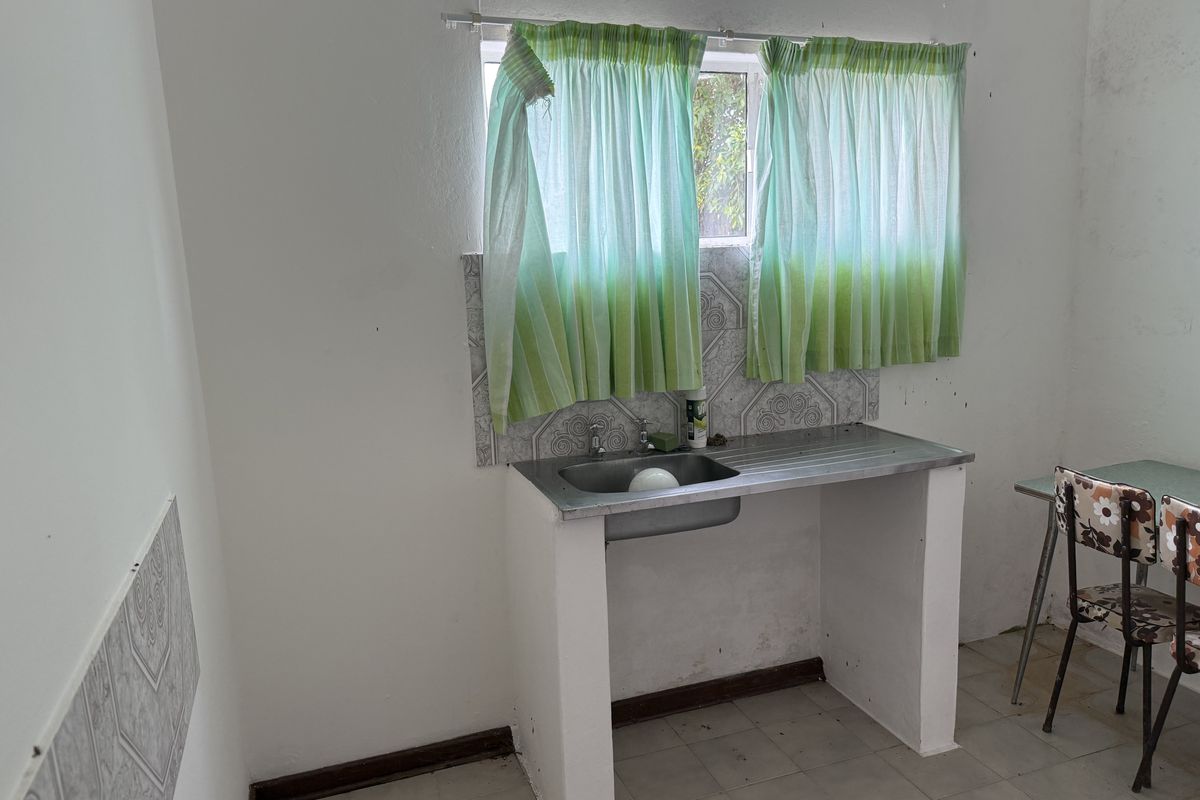 A basic kitchen area featuring a stainless steel sink, tiled splashback, and tiled flooring, requiring cosmetic updates and maintenance.