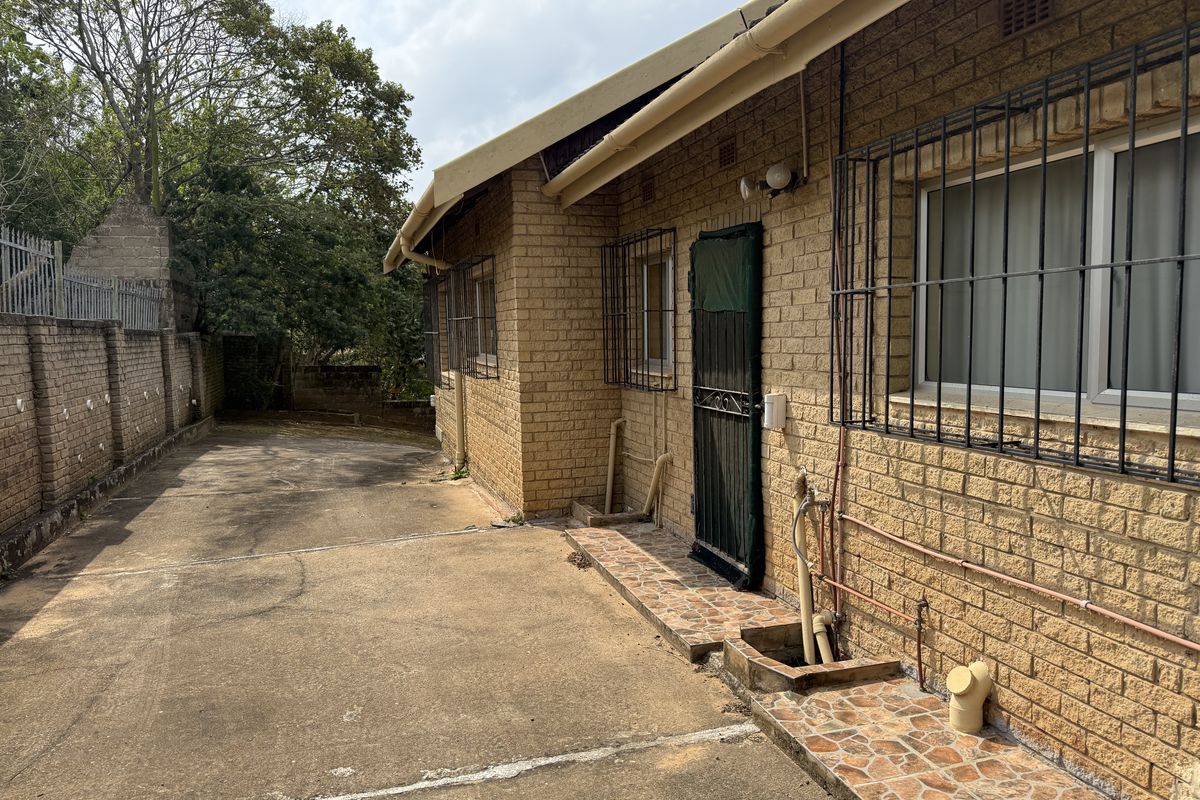 Rear exterior view of the house featuring a face brick facade, security bars on windows, and a concrete driveway area.