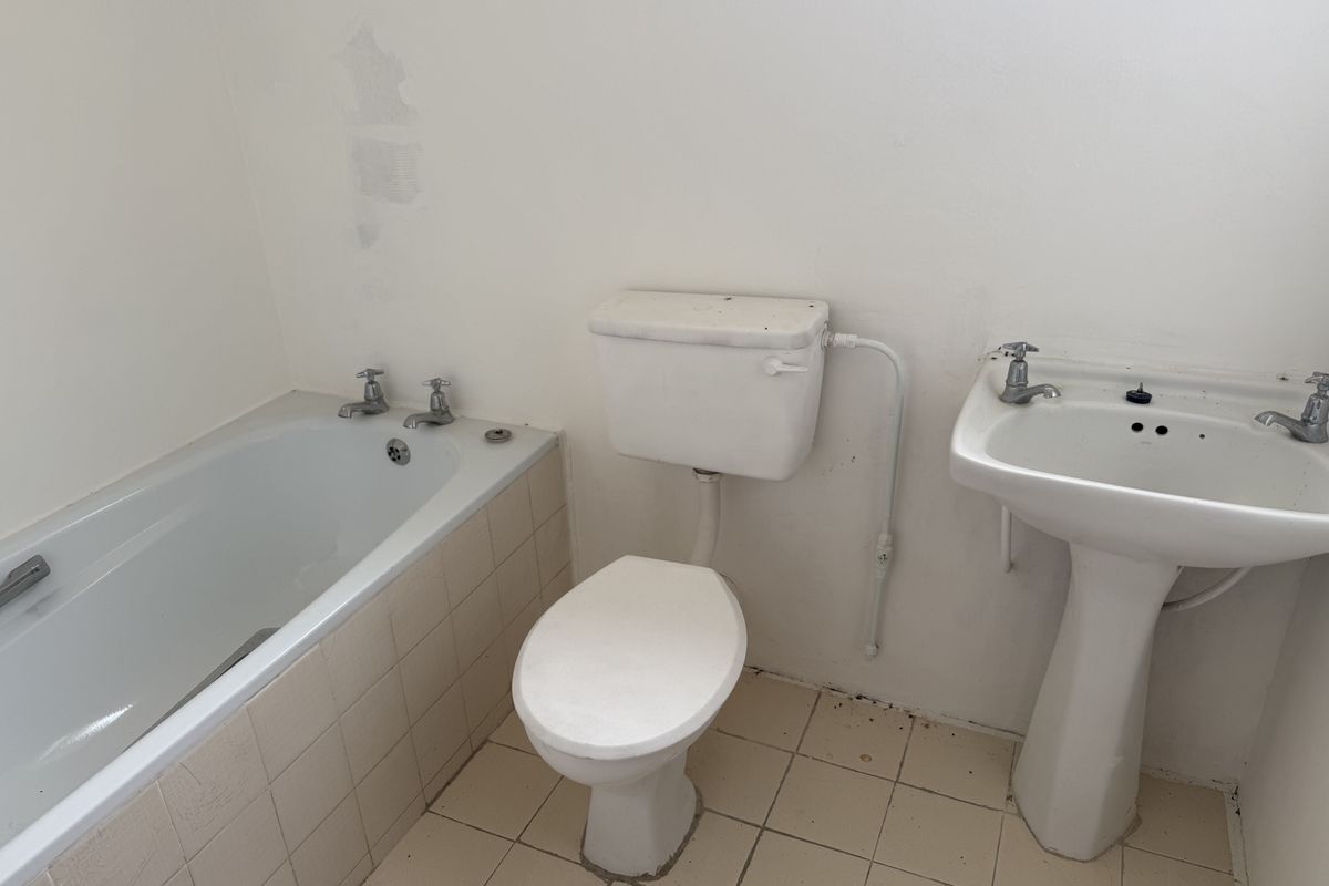 A dated bathroom featuring a standard bathtub, pedestal basin, and toilet, requiring cosmetic updates and repairs to wall finishes and fixtures.