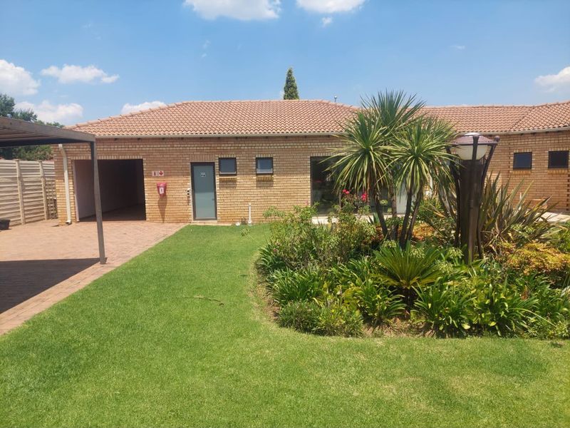 A well-maintained rear exterior view featuring a brick facade, tiled roof, integrated garage, and a neatly landscaped garden with paved areas.