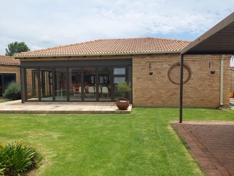 Rear view of the property featuring a brick facade, tiled roof, paved patio area, and large folding glass doors leading into the home.