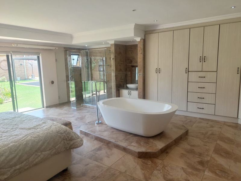 Spacious bedroom featuring an open-plan en-suite with a freestanding bathtub, glass shower, and extensive built-in cabinetry, with direct access to the garden.