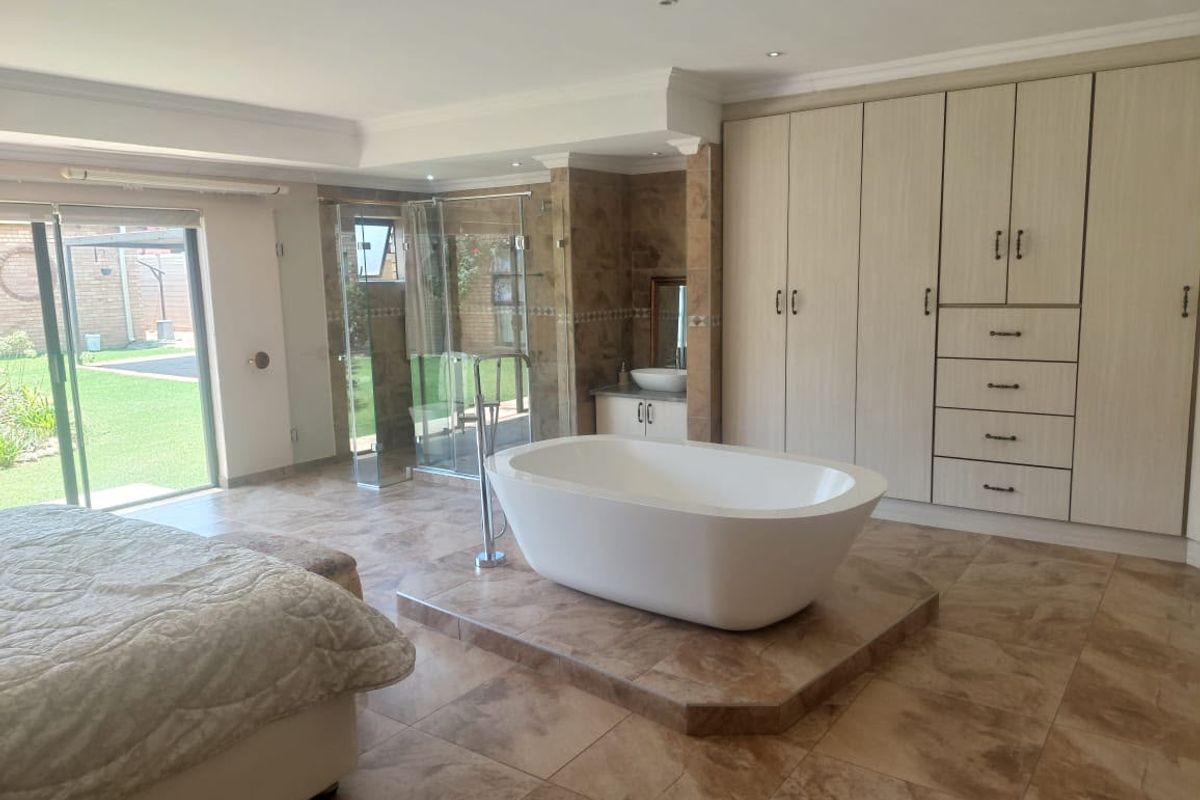 Spacious bedroom featuring an open-plan en-suite with a freestanding bathtub, glass shower, and extensive built-in cabinetry, with direct access to the garden.