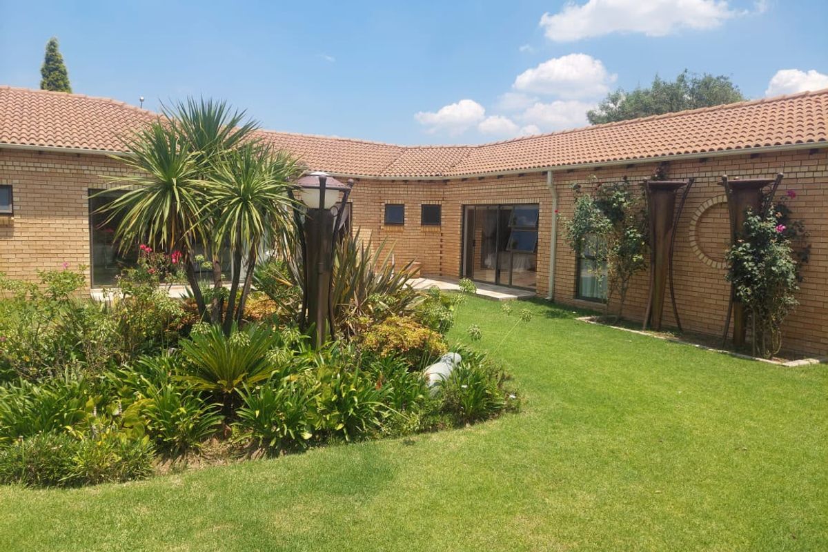 A well-maintained rear garden featuring a lush lawn, established landscaping, and a face brick exterior with sliding glass door access.