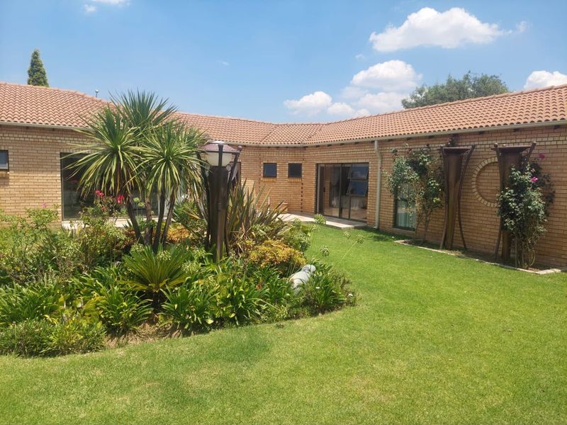 A well-maintained rear garden featuring a lush lawn, established landscaping, and a face brick exterior with sliding glass door access.