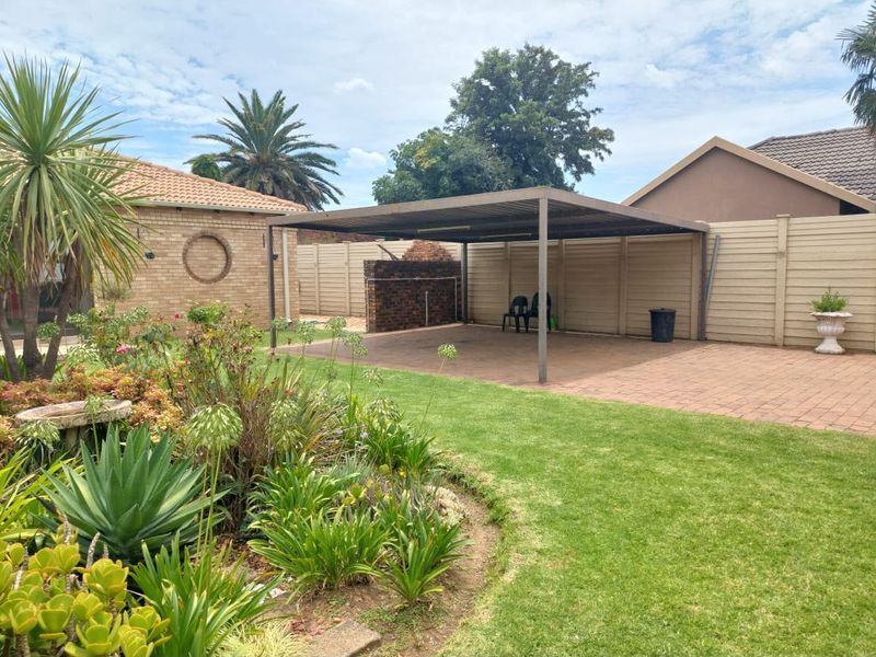 Rear garden area featuring a paved driveway, a functional metal carport, and established landscaping with a brick boundary wall.