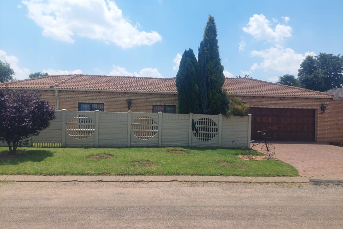 Front view of a single-story brick house featuring a tiled roof, double garage, and a decorative precast concrete boundary wall with a paved driveway.