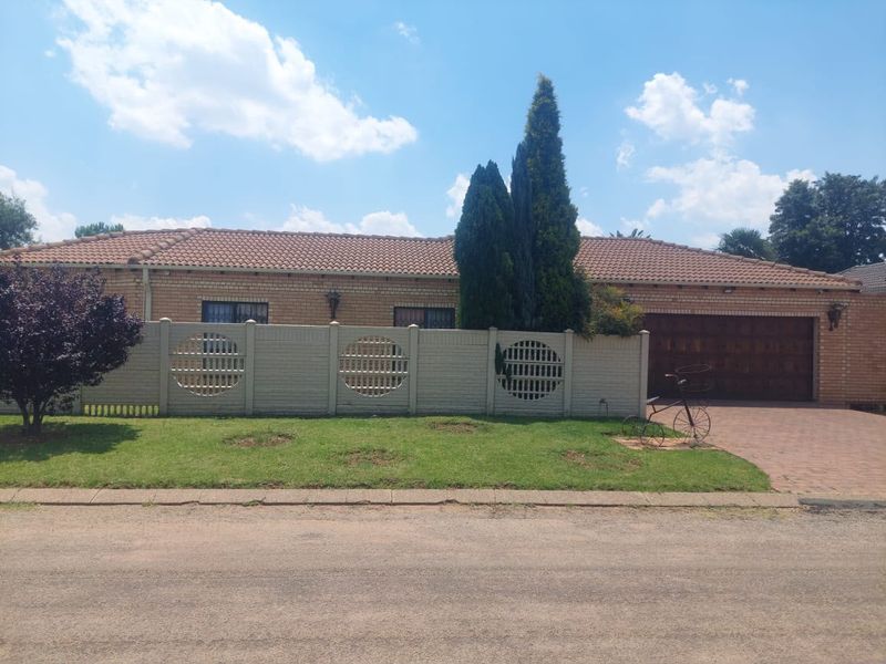 Front view of a single-story brick house featuring a tiled roof, double garage, and a decorative precast concrete boundary wall with a paved driveway.