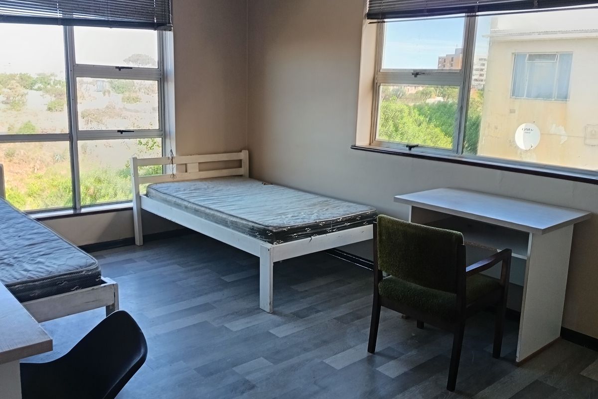 A functional bedroom featuring laminate flooring, large windows with venetian blinds, and ample natural light.