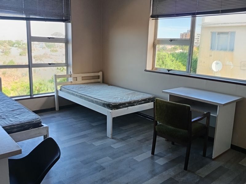 A functional bedroom featuring laminate flooring, large windows with venetian blinds, and ample natural light.
