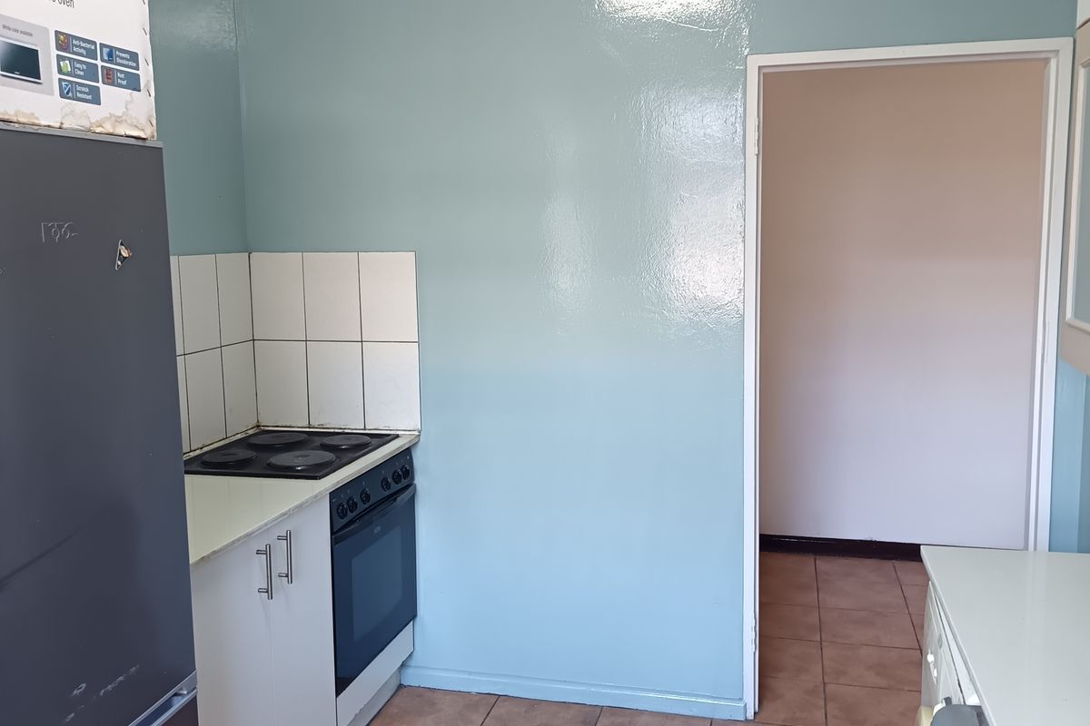 A functional kitchen area featuring built-in cabinetry, an electric hob, oven, and tiled flooring, offering potential for modernization and aesthetic updates.