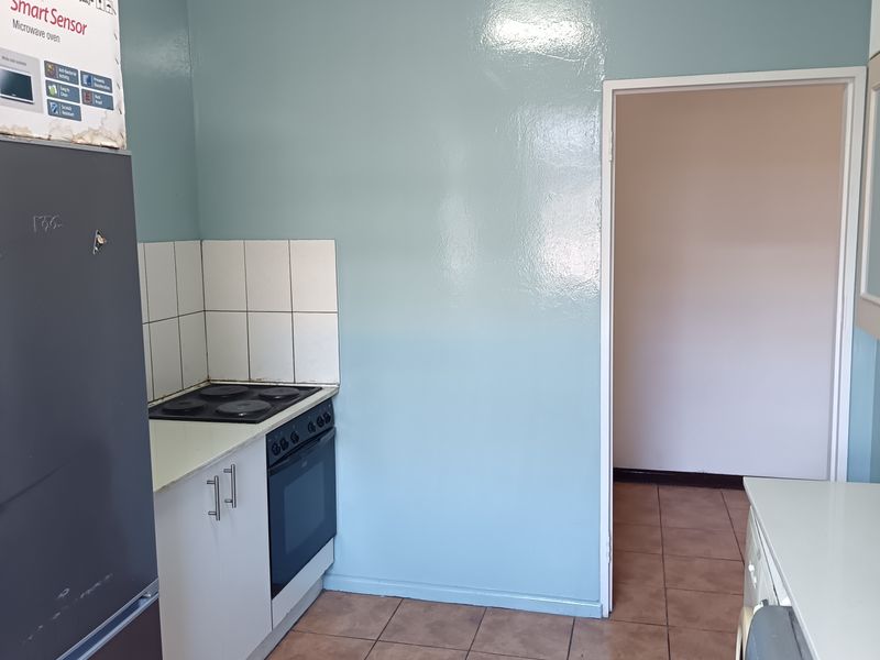 A functional kitchen area featuring built-in cabinetry, an electric hob, oven, and tiled flooring, offering potential for modernization and aesthetic updates.