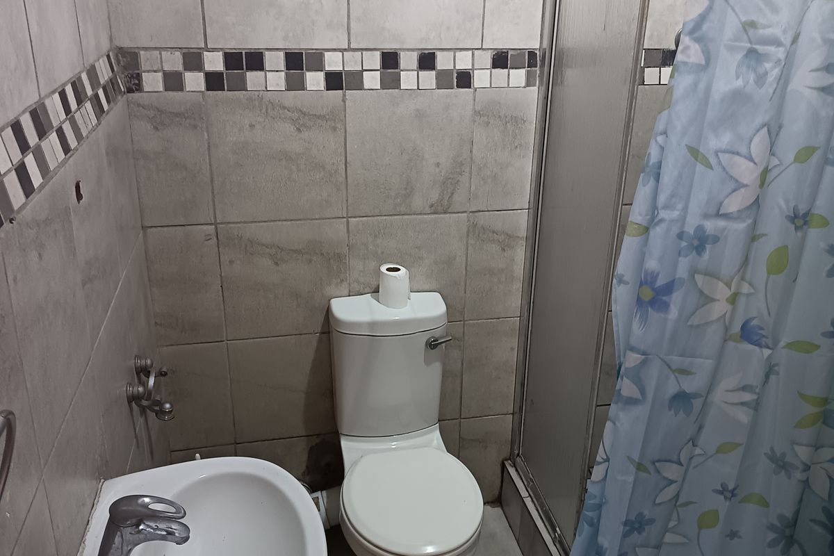 A compact bathroom featuring a pedestal basin, toilet, and shower enclosure with tiled walls and flooring, requiring cosmetic updates to modernize the space.