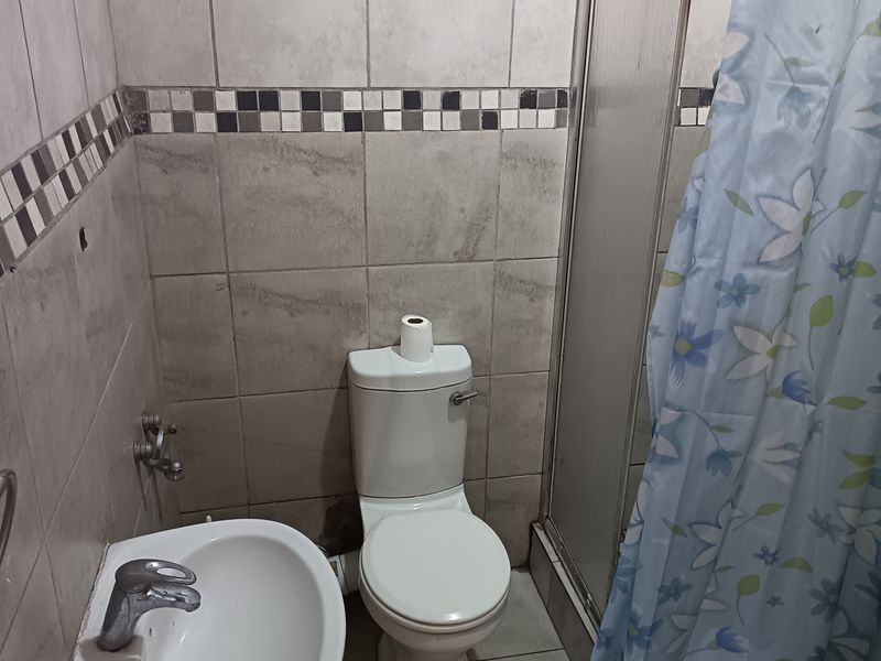 A compact bathroom featuring a pedestal basin, toilet, and shower enclosure with tiled walls and flooring, requiring cosmetic updates to modernize the space.