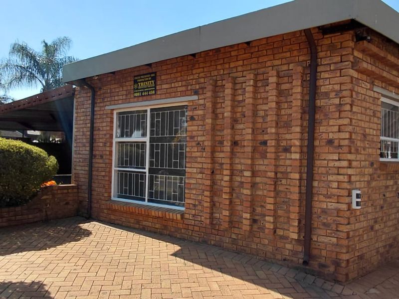 Exterior view of a face brick cottage featuring paved driveway access, security bars on windows, and functional guttering systems.