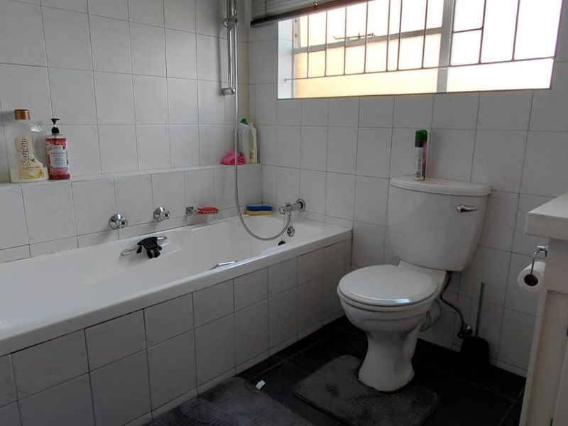 A functional bathroom featuring a built-in bathtub, toilet, and vanity basin with tiled walls and a window providing natural light.