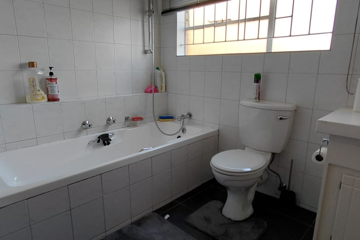 A functional bathroom featuring a built-in bathtub, toilet, and vanity basin with tiled walls and a window providing natural light.