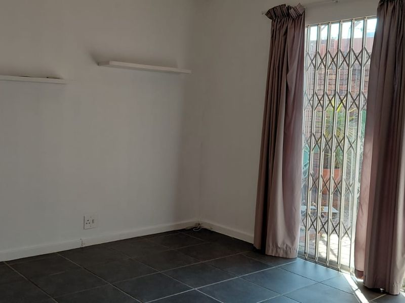 An empty living room featuring dark tiled flooring and a sliding glass door with a security gate leading to the exterior.