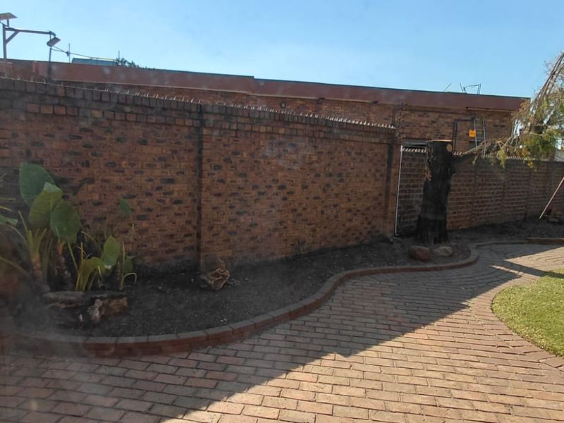 A rear garden area featuring a brick boundary wall with security spikes, paved pathways, and established garden beds.