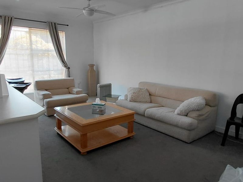 An open-plan living area featuring a kitchen island, ceiling fan, and a combination of tiled and carpeted flooring.