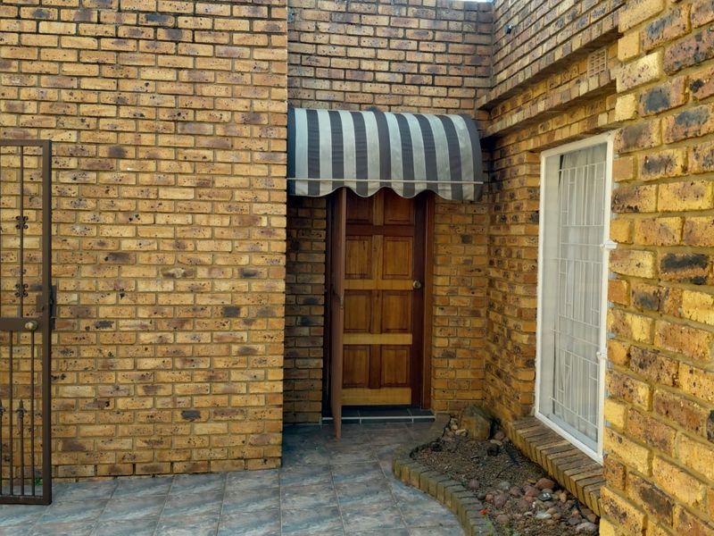 Entrance area featuring a face brick facade, timber door with a striped fabric awning, and a tiled patio with a security gate.